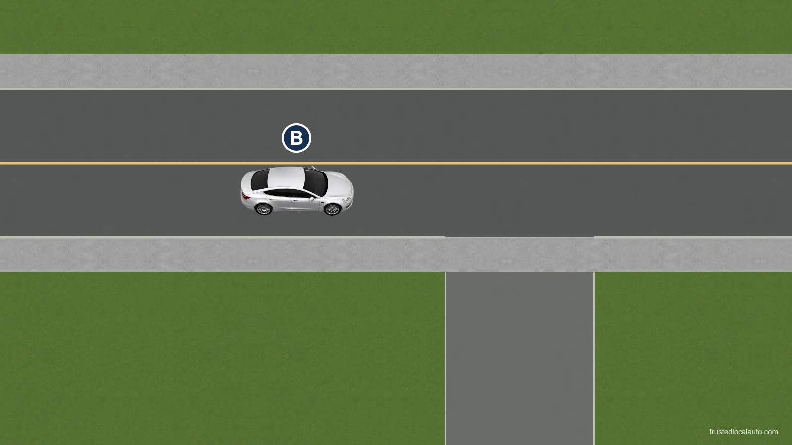 An empty driveway crosses a continuous sidewalk beside a road. Silver B is on the through road.