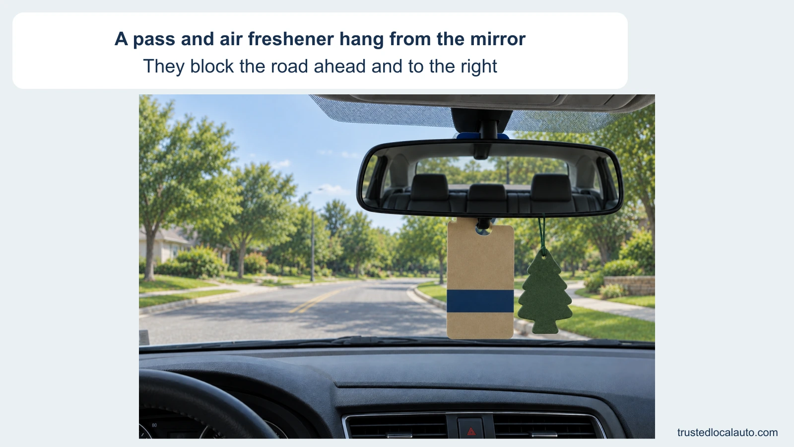 A large tan parking pass and a green air freshener hang below the rearview mirror. They obscure the roadway ahead and to the right through the windshield.